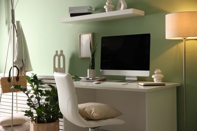 Home office. Comfortable workplace with desk, computer and lamp near light green wall in room