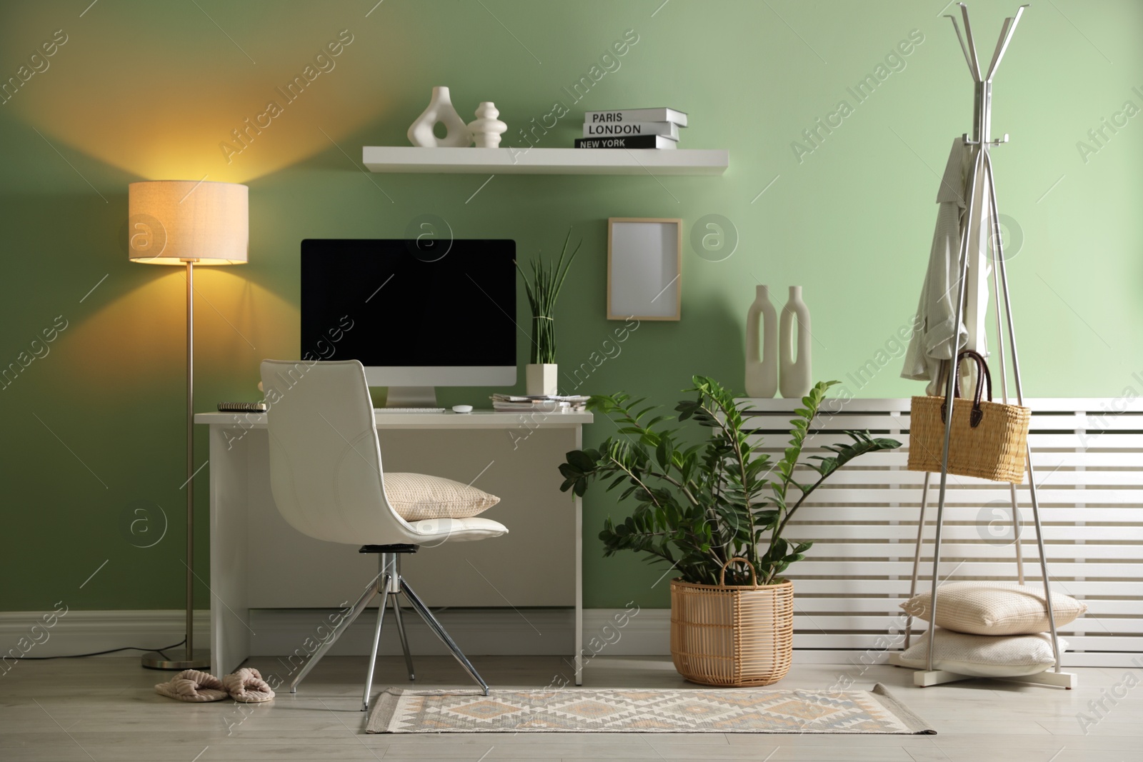 Photo of Home office. Comfortable workplace with desk, computer and lamp near light green wall in room