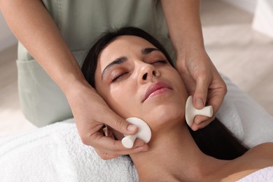 Photo of Young woman receiving facial massage with spa stones in salon