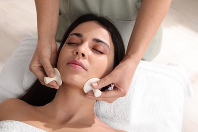 Photo of Young woman receiving facial massage with spa stones in salon