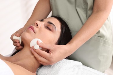 Photo of Young woman receiving facial massage with spa stones in salon