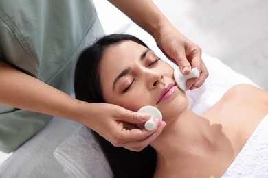 Photo of Young woman receiving facial massage with spa stones in salon