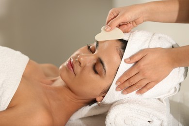 Photo of Young woman receiving facial massage with gua sha tool in spa salon