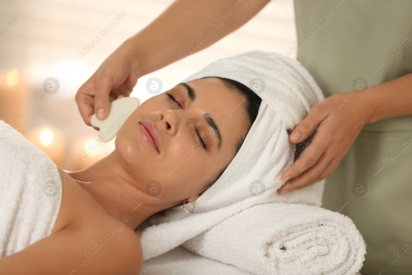 Photo of Young woman receiving facial massage with gua sha tool in spa salon