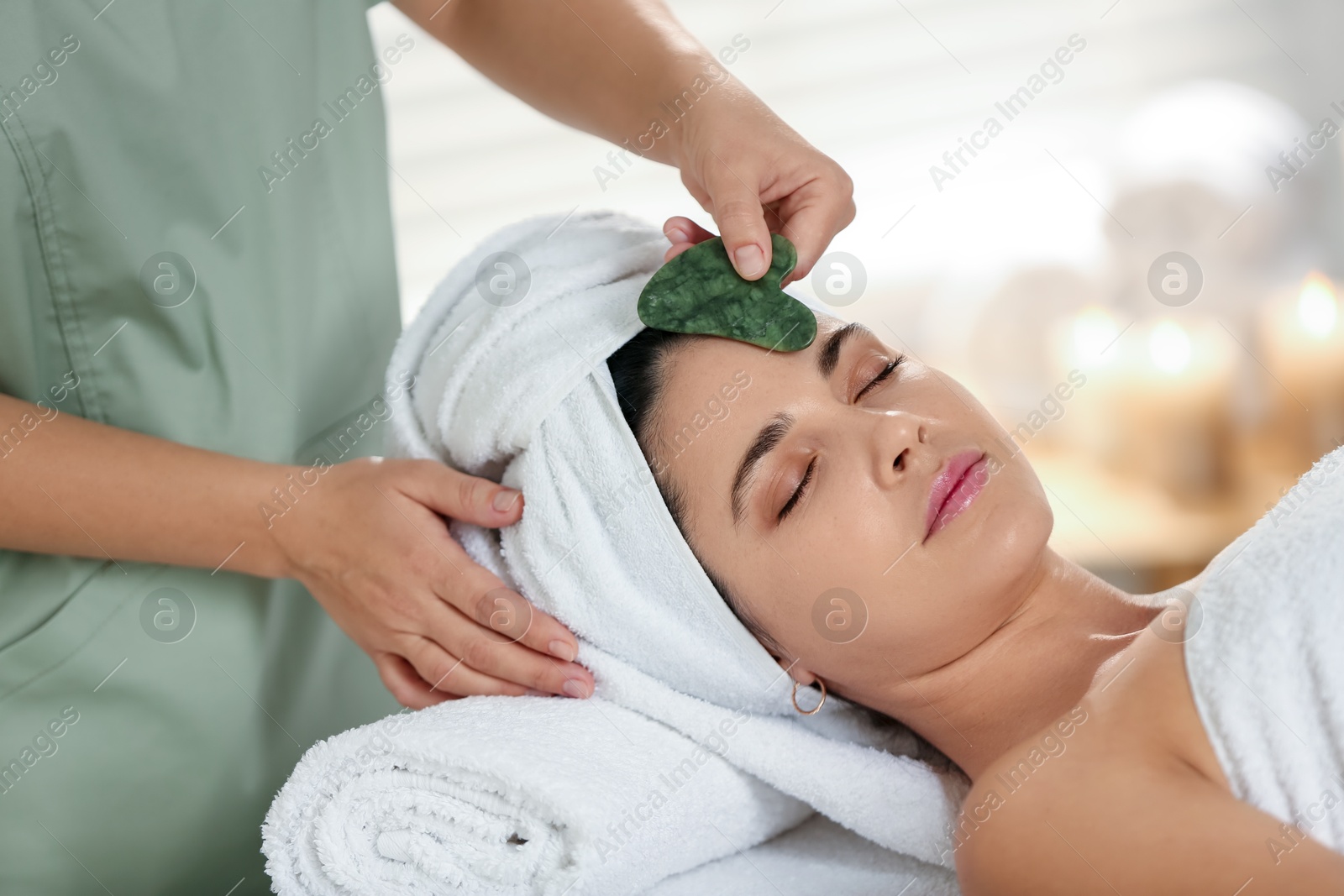 Photo of Young woman receiving facial massage with gua sha tool in spa salon