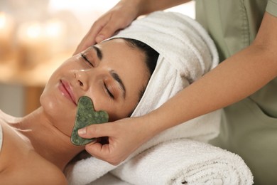 Photo of Young woman receiving facial massage with gua sha tool in spa salon