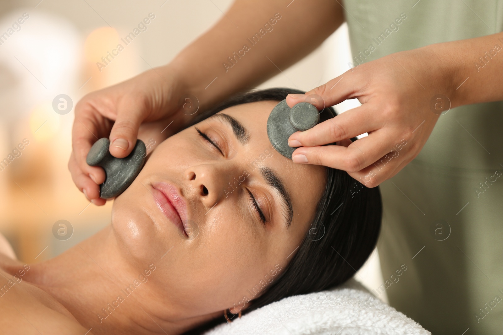 Photo of Young woman receiving facial massage with spa stones in salon