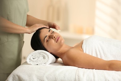 Photo of Young woman receiving facial massage with gua sha tool in spa salon