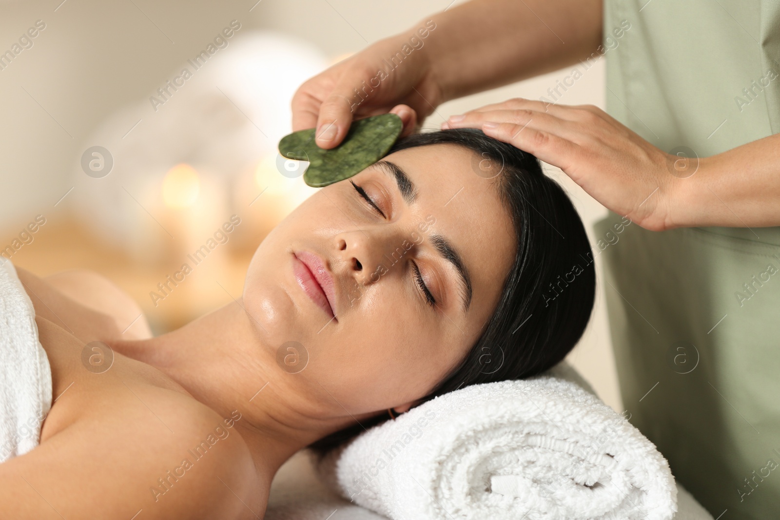 Photo of Young woman receiving facial massage with gua sha tool in spa salon