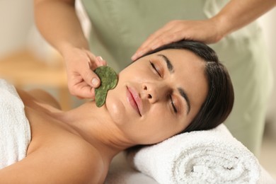 Photo of Young woman receiving facial massage with gua sha tool in spa salon