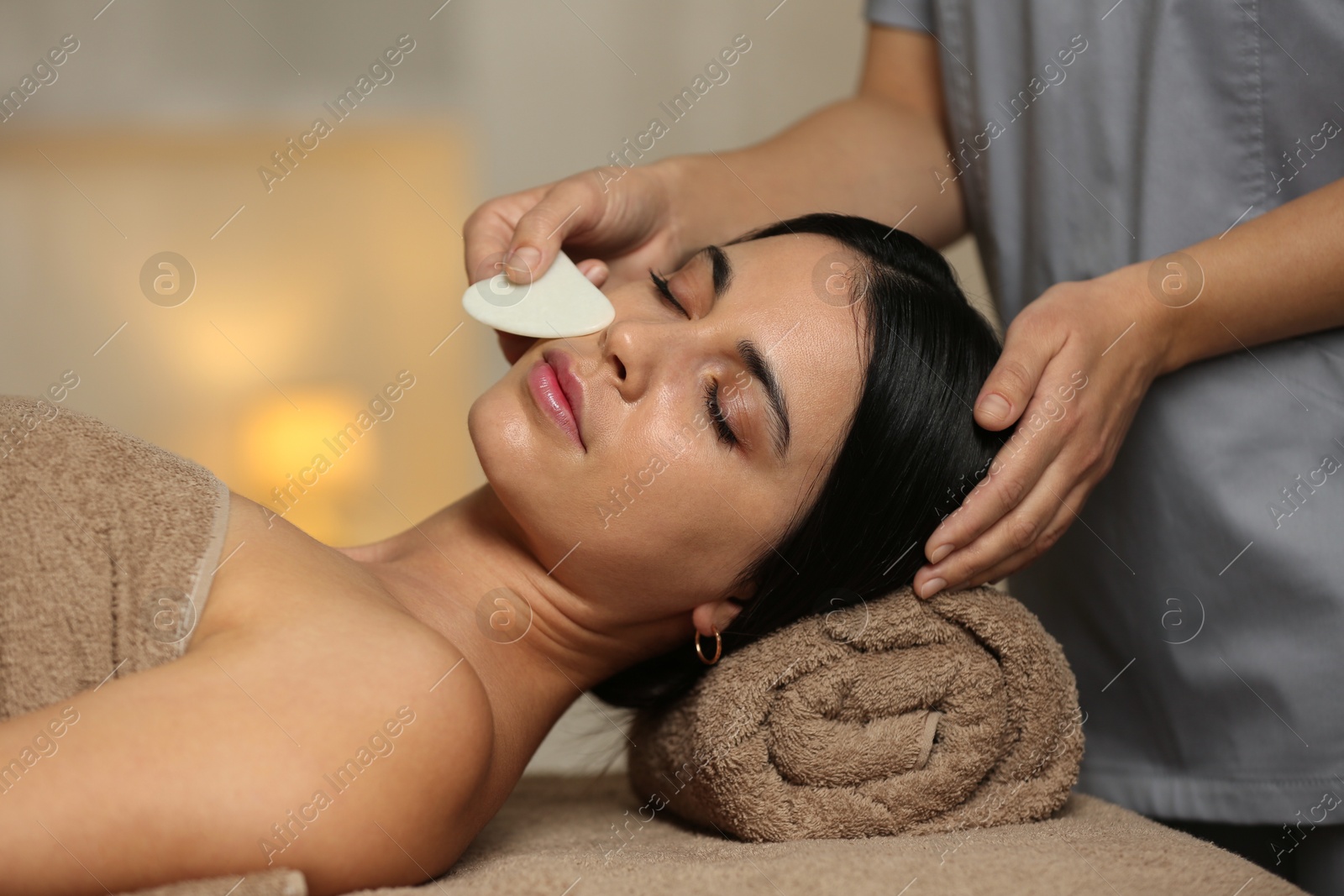 Photo of Young woman receiving facial massage with gua sha tool in spa salon