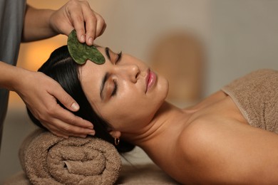 Photo of Young woman receiving facial massage with gua sha tool in spa salon