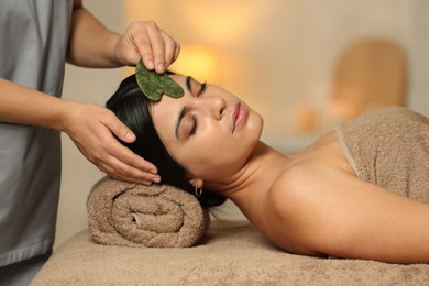 Photo of Young woman receiving facial massage with gua sha tool in spa salon