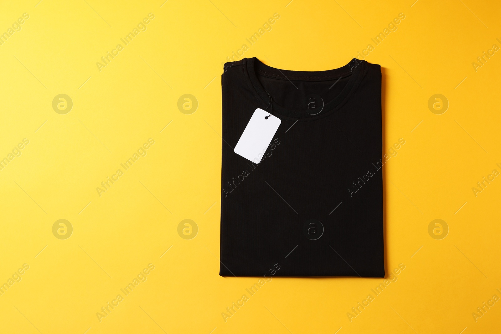 Photo of Blank black t-shirt on yellow background, top view. Mockup for design