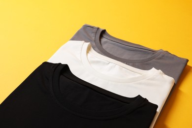 Photo of Different blank t-shirts on yellow background, closeup