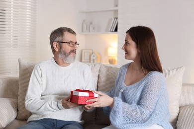 Photo of Happy daughter presenting her father with gift on sofa at home