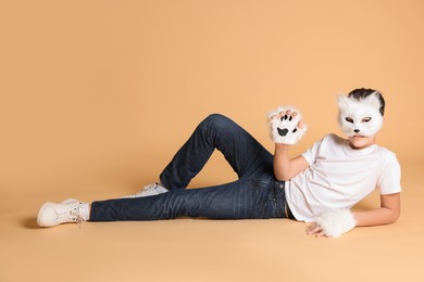 Photo of Quadrobics. Boy wearing cat mask and gloves on beige background