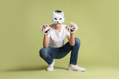 Photo of Quadrobics. Boy wearing cat mask and gloves on pale olive background