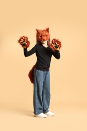 Photo of Quadrobics. Girl wearing fox mask, tail and gloves on beige background