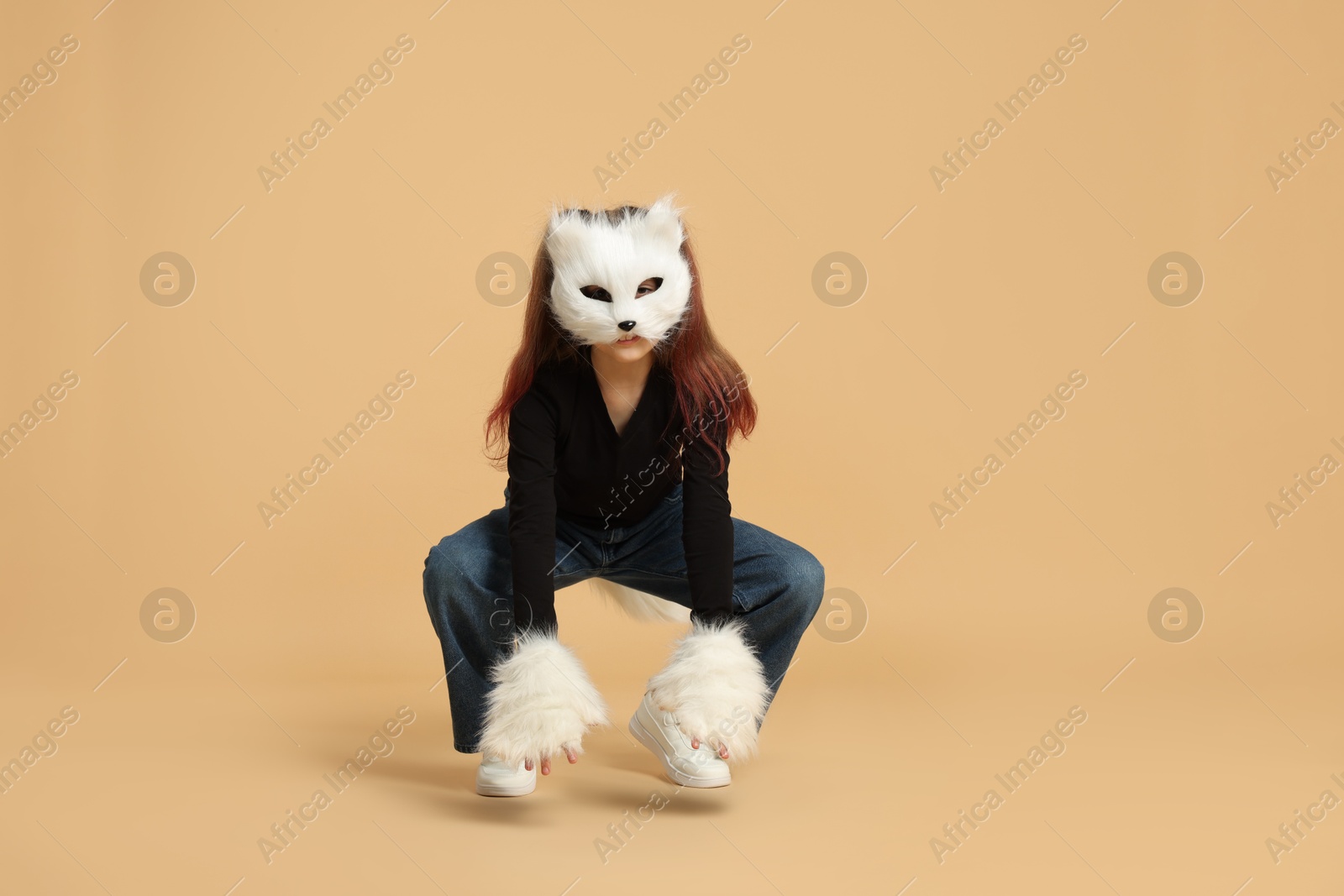 Photo of Quadrobics. Girl wearing cat mask, tail and gloves on beige background