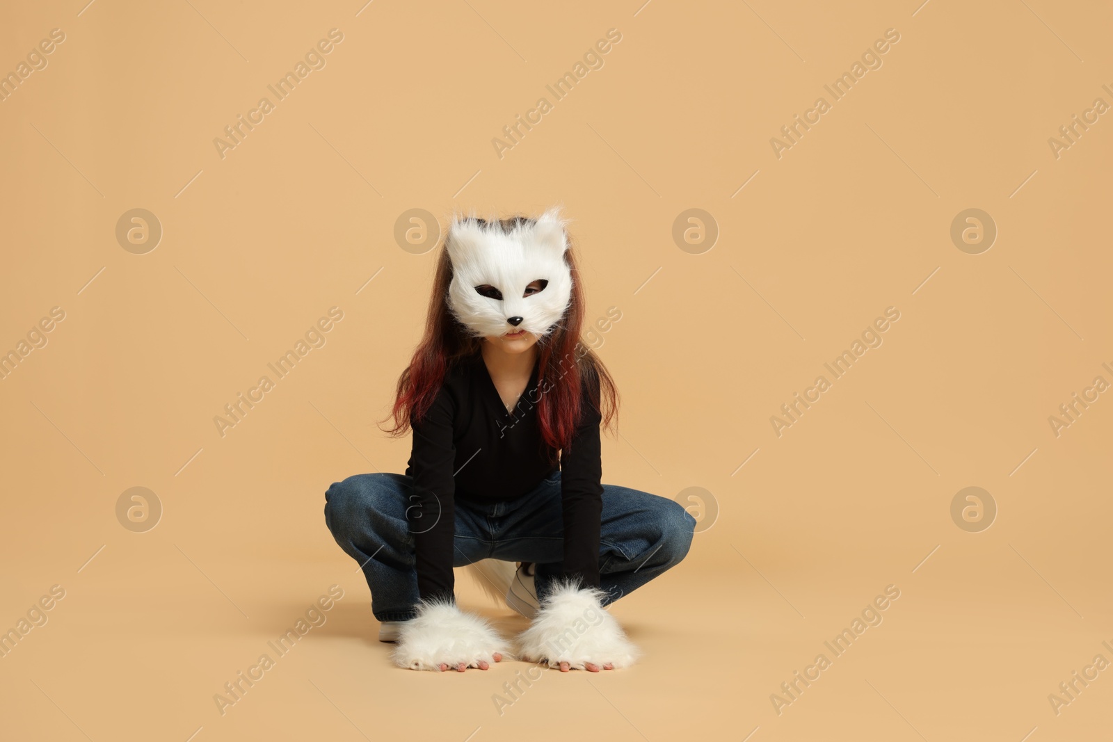 Photo of Quadrobics. Girl wearing cat mask, tail and gloves on beige background