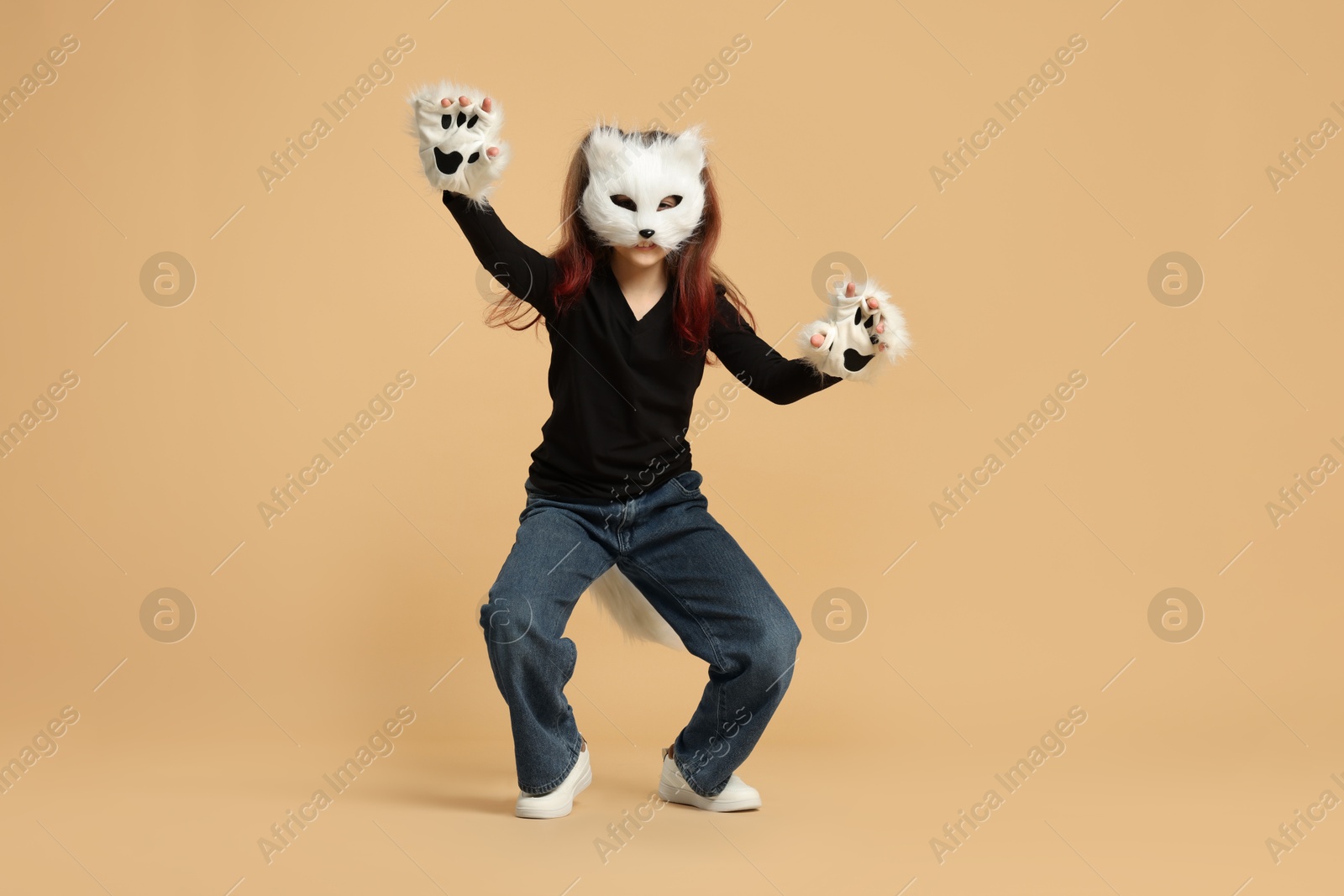 Photo of Quadrobics. Girl wearing cat mask, tail and gloves on beige background