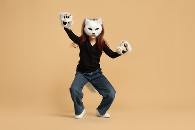 Photo of Quadrobics. Girl wearing cat mask, tail and gloves on beige background