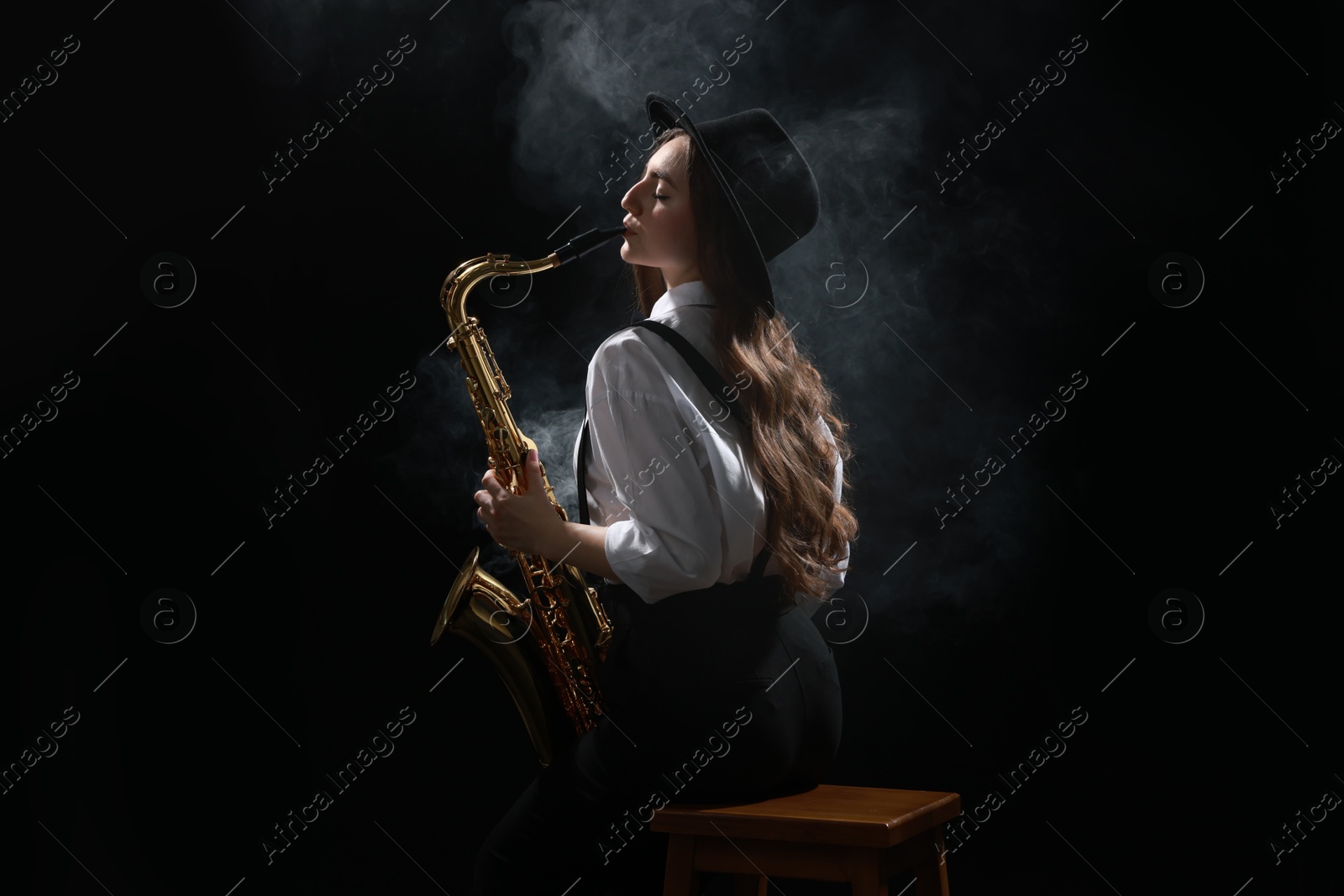 Photo of Professional musician playing saxophone on dark background with smoke