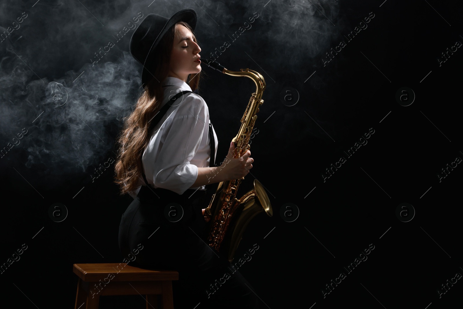 Photo of Professional musician playing saxophone on dark background with smoke