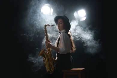 Photo of Professional musician playing saxophone on dark background with lights and smoke