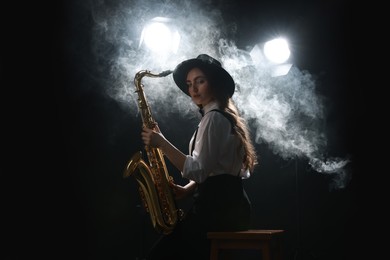 Photo of Professional musician playing saxophone on dark background with lights and smoke