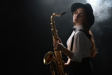 Photo of Professional musician playing saxophone on dark background with lights and smoke. Space for text