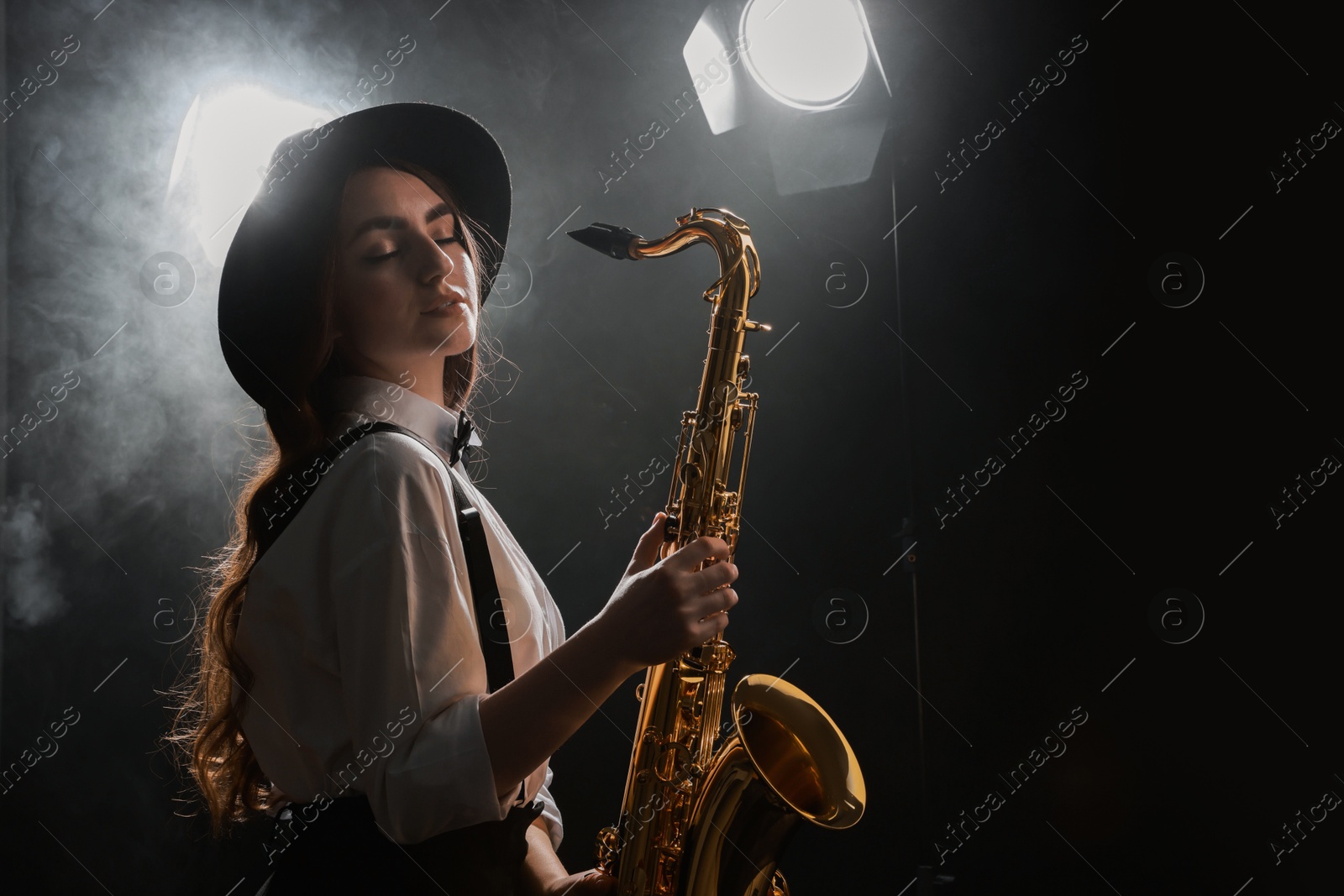 Photo of Professional musician playing saxophone on dark background with lights and smoke. Space for text