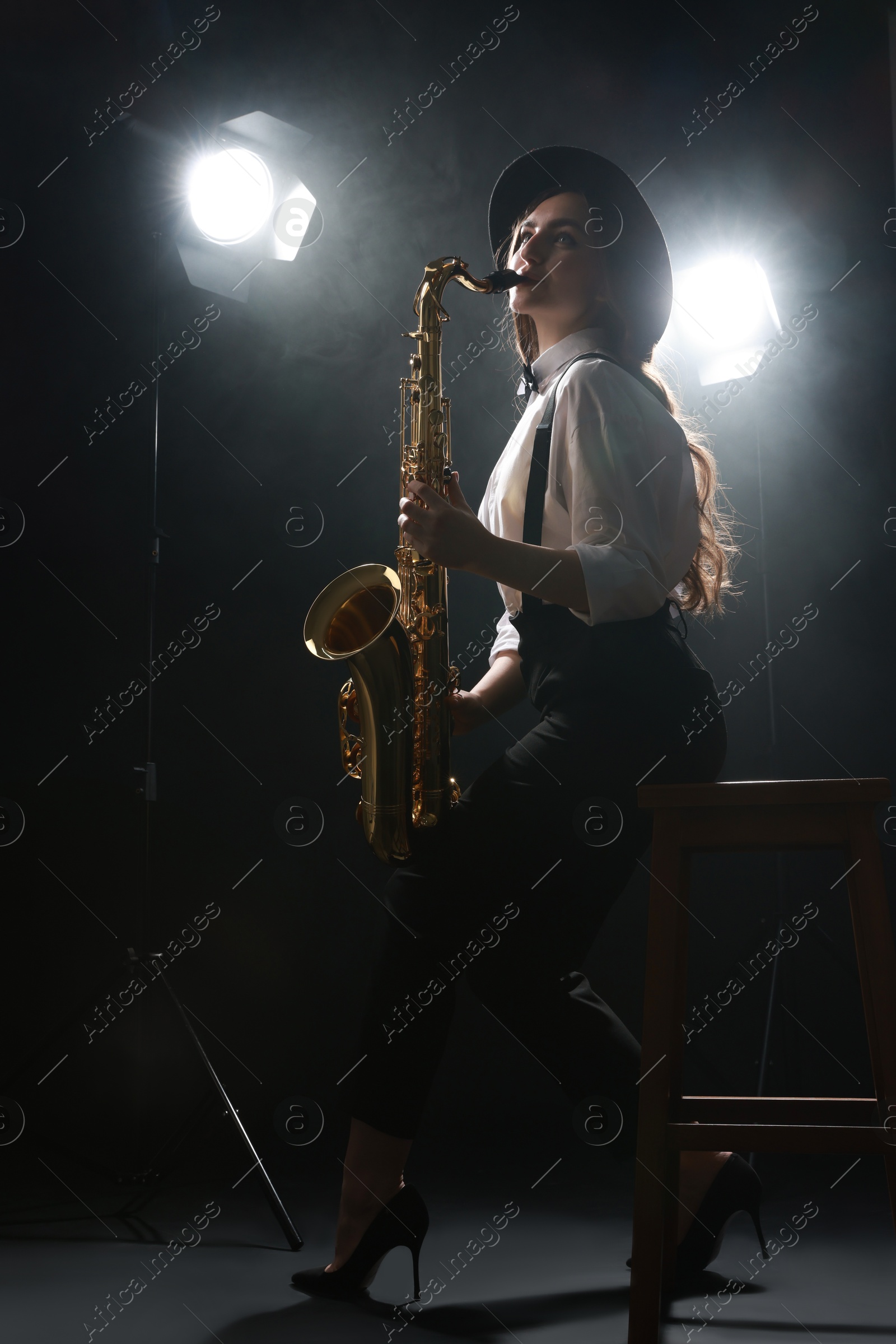 Photo of Professional musician playing saxophone on dark background with lights and smoke