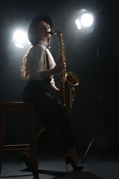 Photo of Professional musician playing saxophone on dark background with lights and smoke