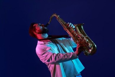 Photo of Professional musician playing saxophone on color background with neon lights