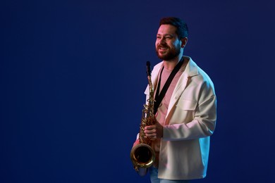 Photo of Professional musician with saxophone on blue background. Space for text