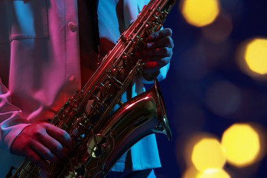 Photo of Professional musician playing saxophone on blue background with blurred lights, closeup. Bokeh effect