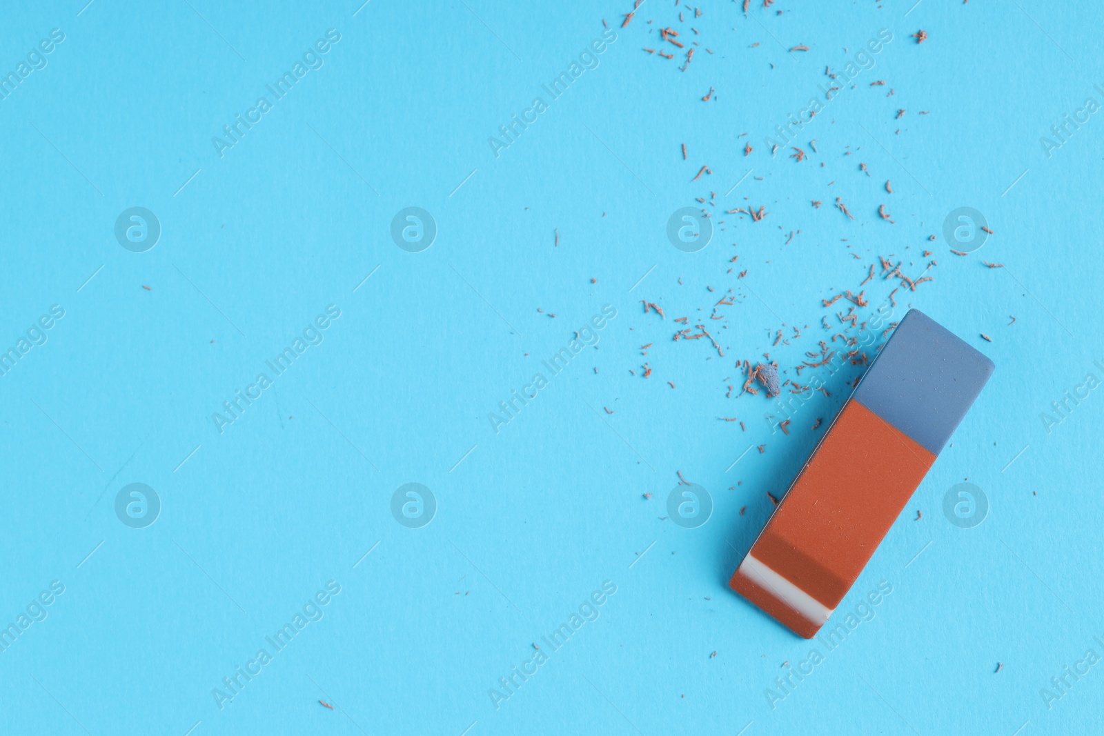 Photo of One eraser and scraps on light blue background, top view. Space for text