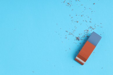 Photo of One eraser and scraps on light blue background, top view. Space for text