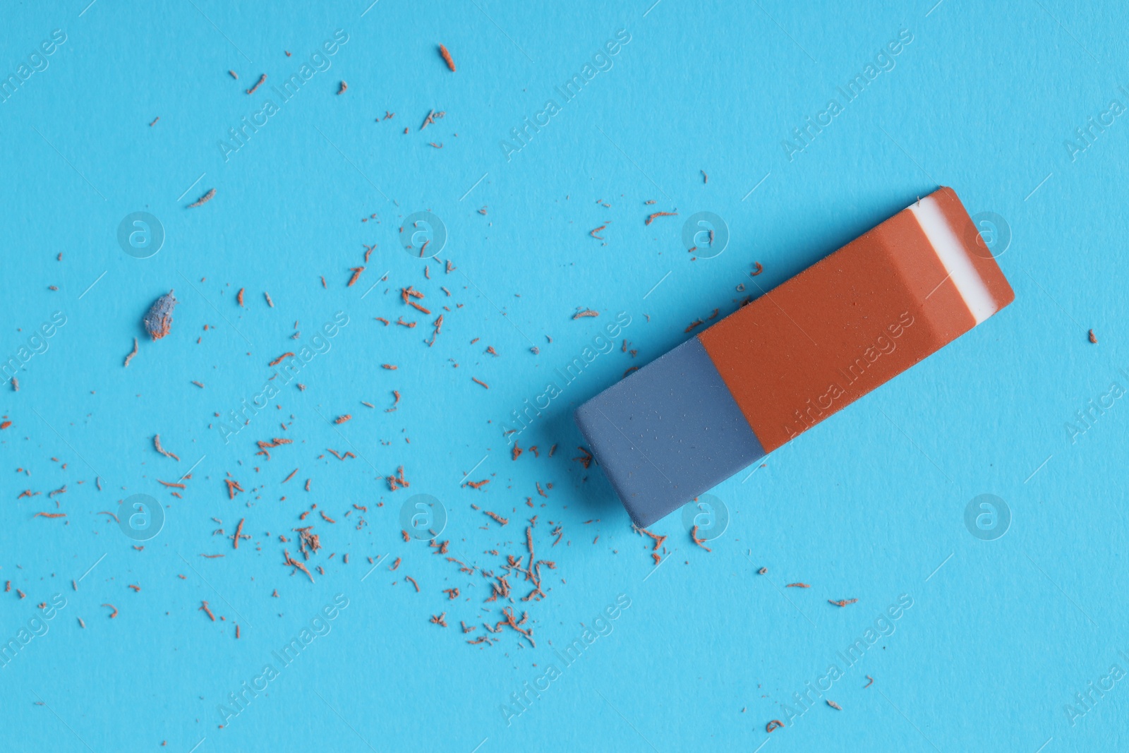 Photo of One eraser and scraps on light blue background, top view