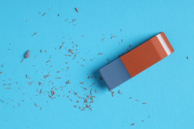 Photo of One eraser and scraps on light blue background, top view