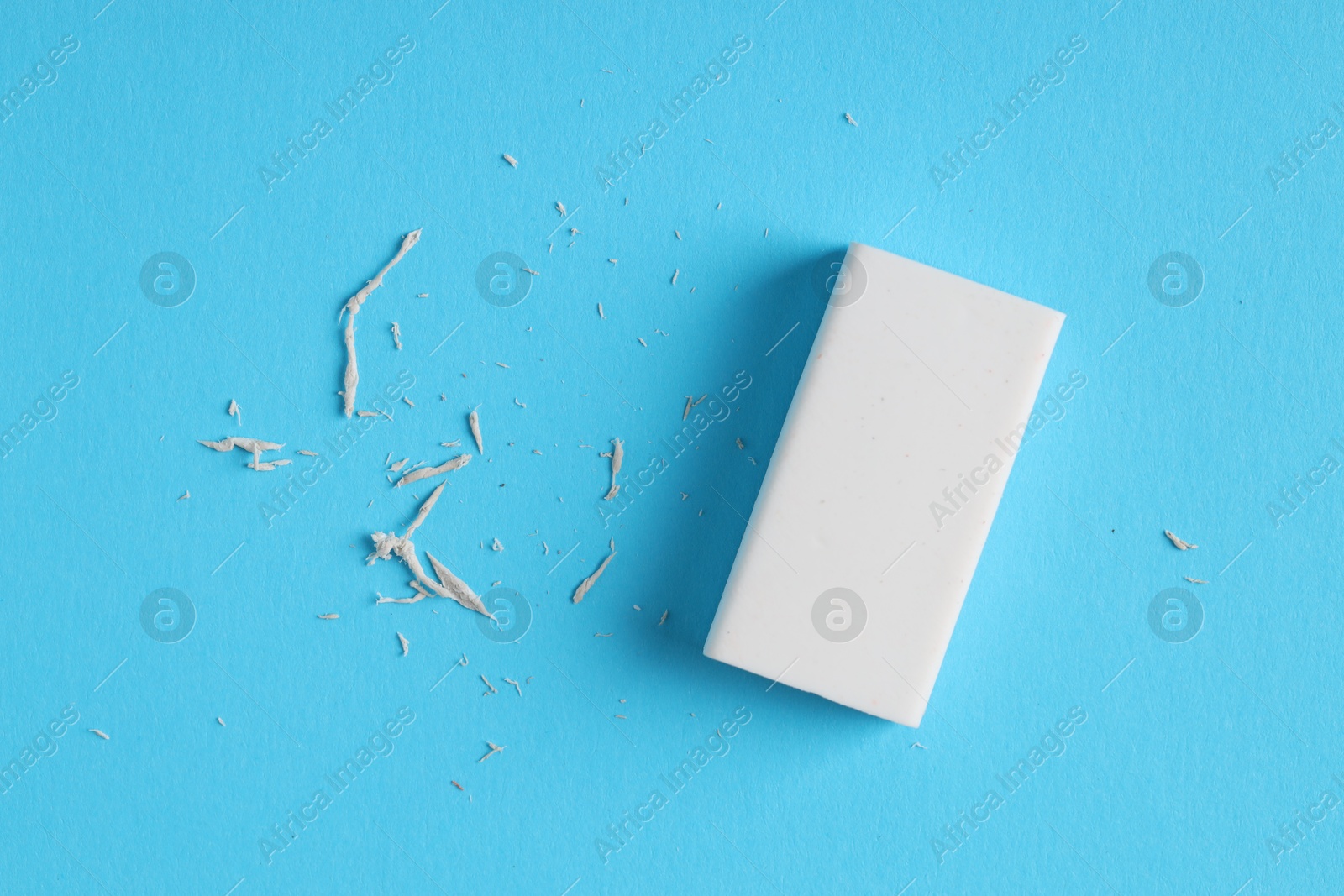 Photo of One eraser and scraps on light blue background, top view