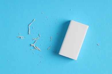 Photo of One eraser and scraps on light blue background, top view