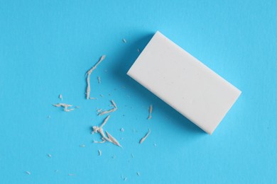 Photo of One eraser and scraps on light blue background, top view