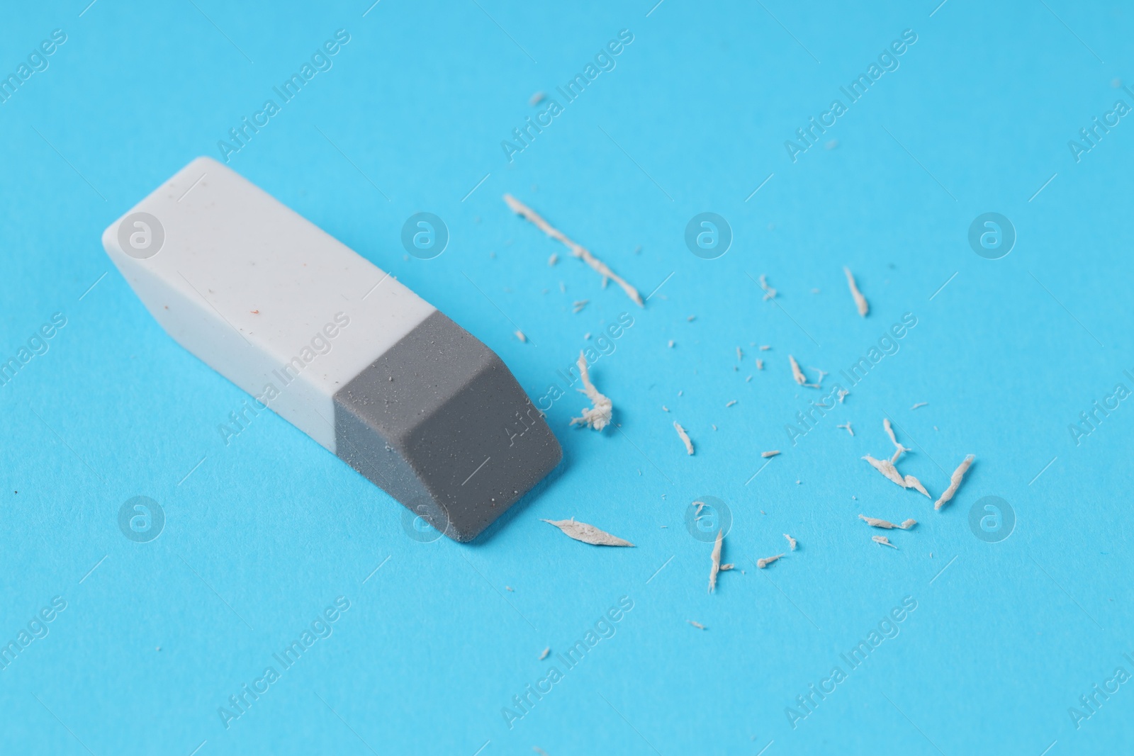 Photo of One eraser and scraps on light blue background, closeup