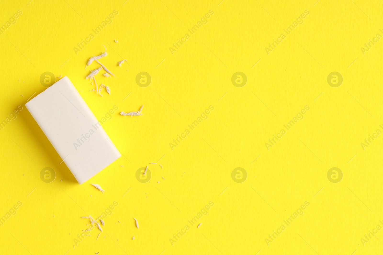 Photo of One eraser and scraps on yellow background, top view. Space for text