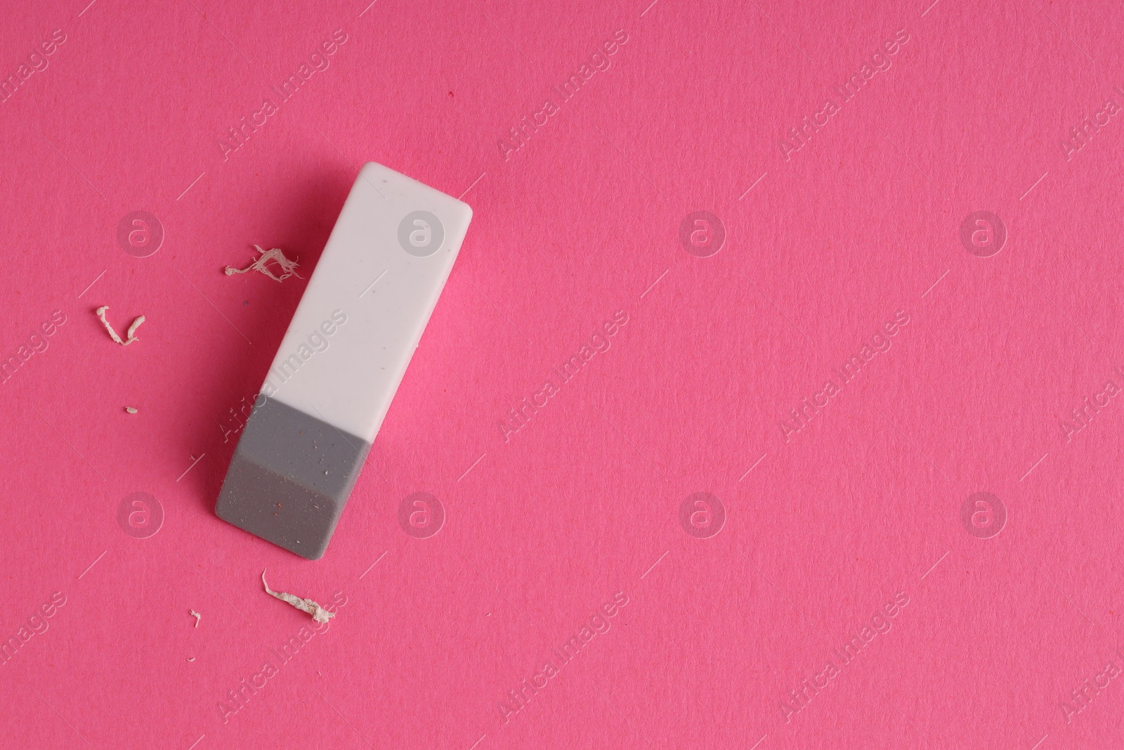 Photo of One eraser and scraps on pink background, top view. Space for text