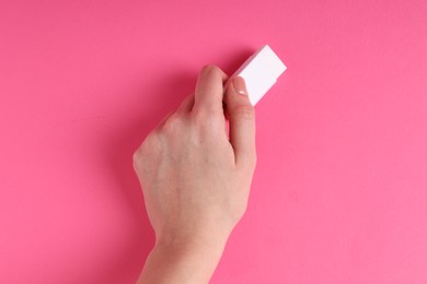 Photo of Woman using eraser on pink background, closeup