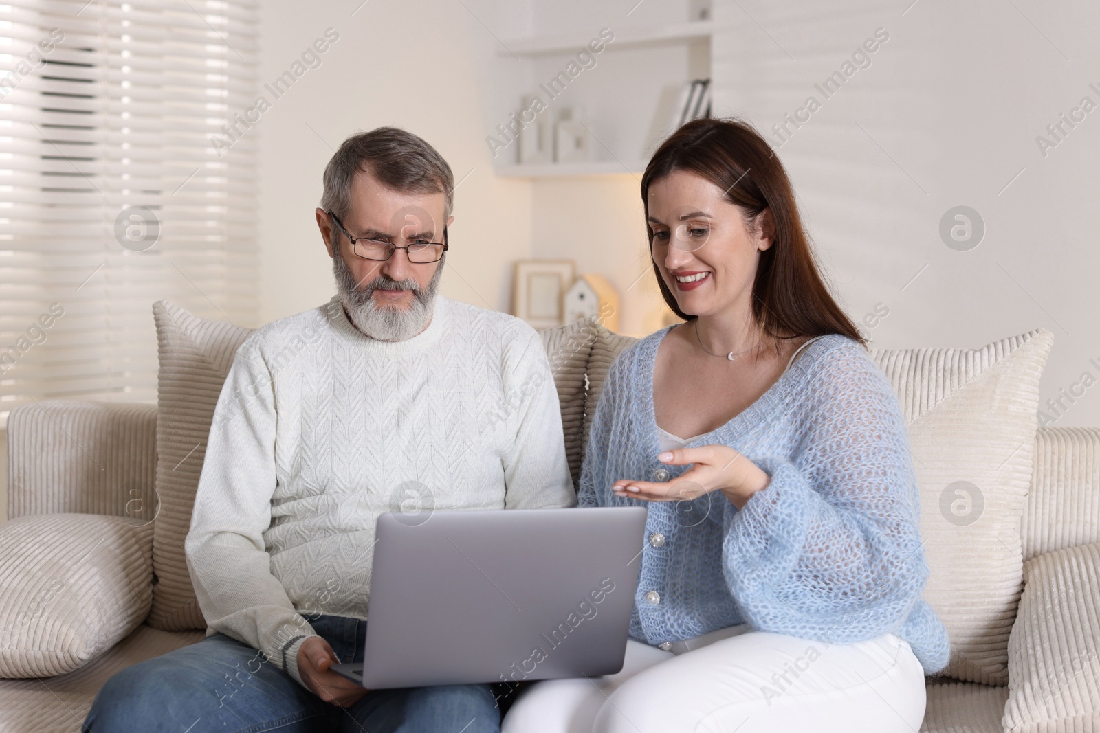 Photo of Happy daughter explaining her father how to use laptop on sofa at home